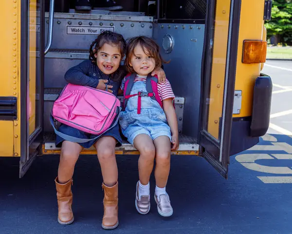 Child with down syndrome sitting on school bus steps with friend