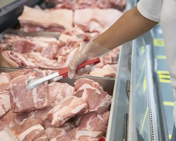 Tongs grabbing raw pork