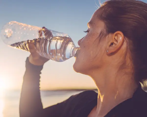 A woman drinks water from a clear disposable plastic water bottle.