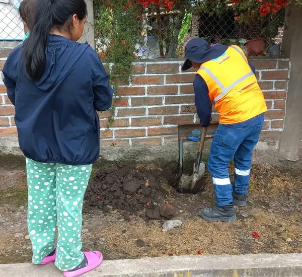 Photo of a worker digging a hole in front of a residence in Ecuador with an onlooker nearby