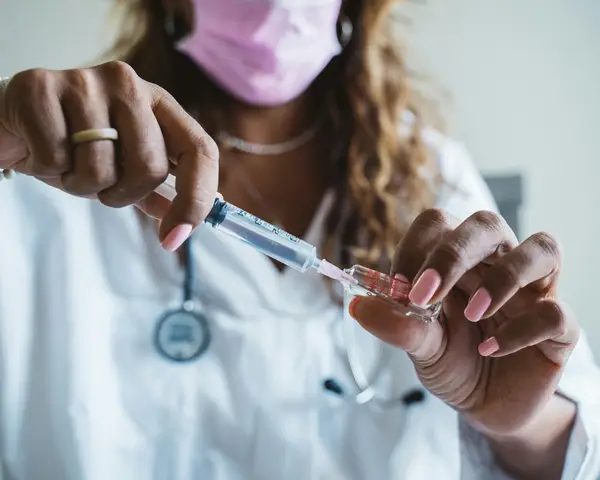 A medical professional in a surgical mask extracts a substance with a syringe. 