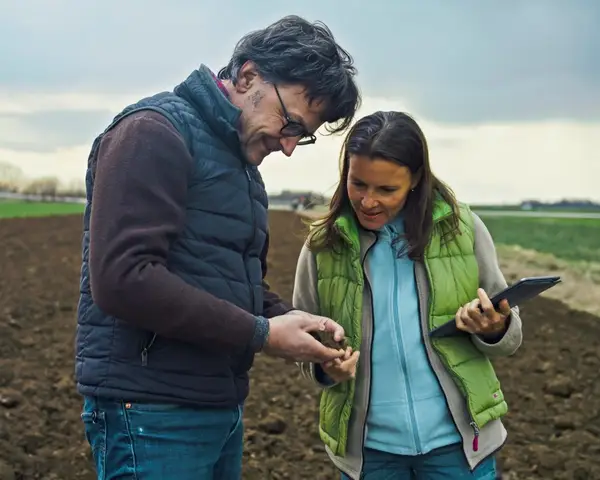 A man and a woman check a tablet while standing in a farm field.