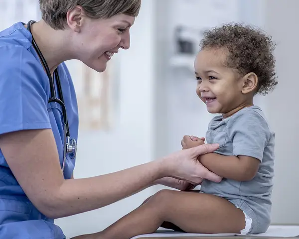 A doctor plays with a baby on an exam table.