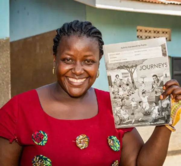 Rachel Nabbanja, a teacher at Kiiya Primary School in Luwero, Uganda, poses for a portrait with classroom material developed through Journeys. Photo: Katie G. Nelson for RTI International