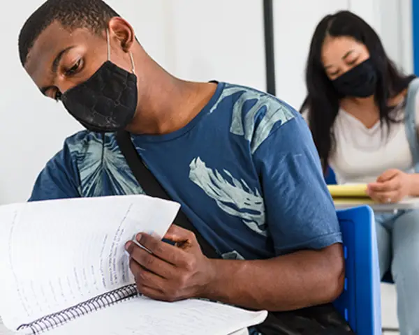 student with mask looking at notebook