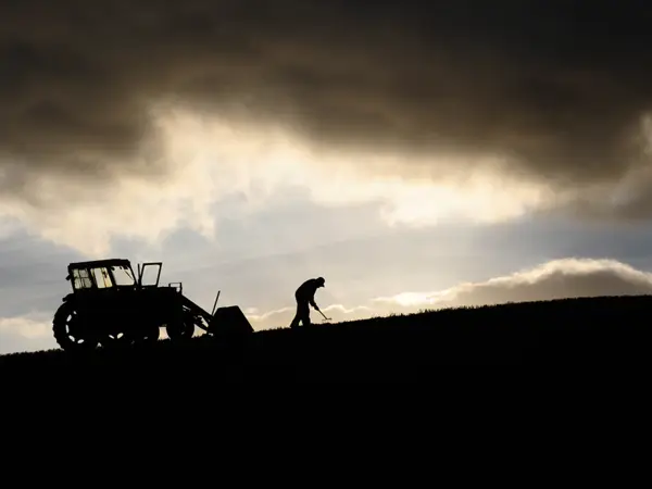 Photo of a farm worker and tractor silhouetted 