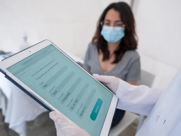 Clinician holding tablet while masked patient sits
