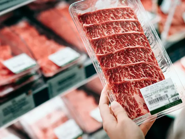 Hand holding a package of red meat in the meat section at a grocery story