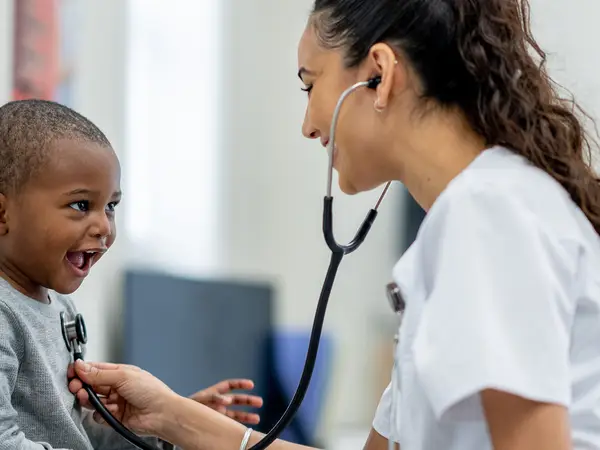 A child smiles while a doctor checks his heartbeat with a stethoscope.