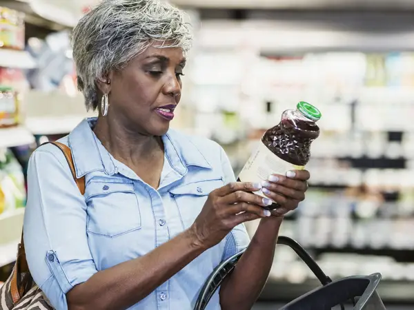 A woman checks the label on a bottle of juice in a grocery store.