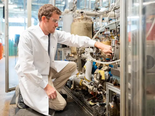 man in lab coat turning knob on industrial equipment