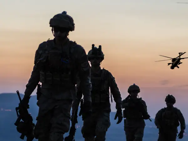 Soldiers march forward at dusk across a flat, open landscape.