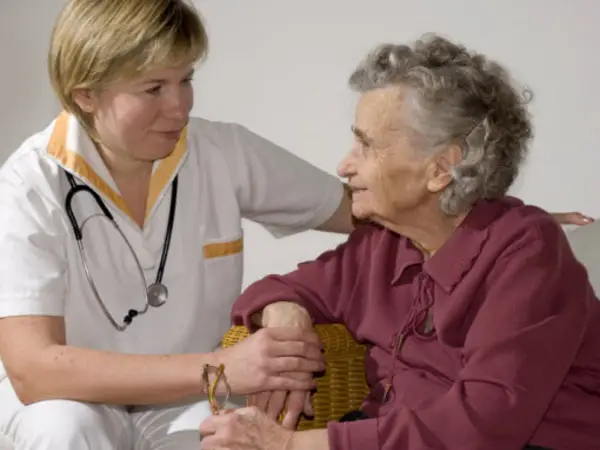 A caregiver gently interacts with an elderly woman in a comfortable, nurturing setting.