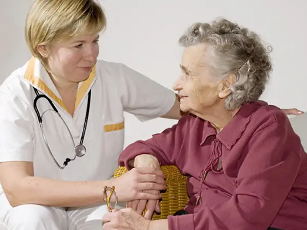 A caregiver gently interacts with an elderly woman in a comfortable, nurturing setting.