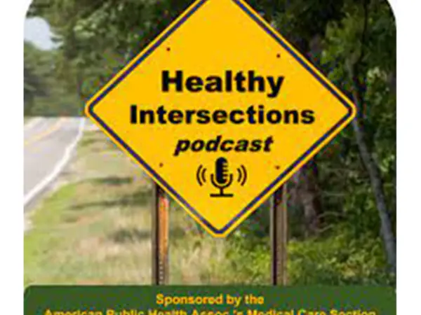 Yellow diamond-shaped road sign reads "Healthy Intersections podcast" with a microphone, against roadside greenery.
