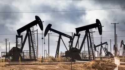 Oil pumpjacks dot a dry field beneath a stormy sky.
